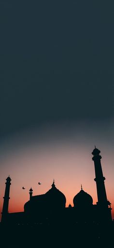 the silhouette of two tall buildings against a dark sky at sunset or dawn with an airplane flying in the distance