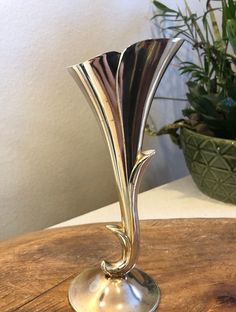 a silver vase sitting on top of a wooden table next to a potted plant