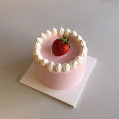 a strawberry on top of a pink cake with white frosting in the shape of a circle