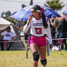 a female rollerblader in pink shorts and knee pads walking on the grass with an umbrella behind her