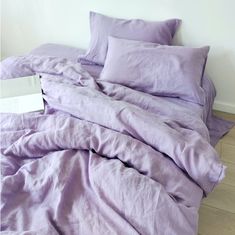 an unmade bed with purple sheets and pillows on top of it, next to a white wall