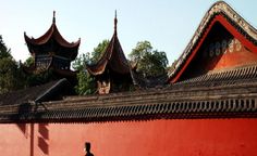 a man walking down the street in front of a red wall and some tall buildings