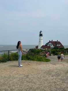 a woman standing on top of a dirt field next to the ocean and a light house