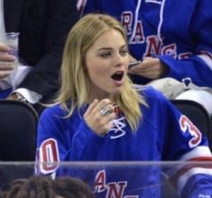 a woman is sitting in the stands at a hockey game and making a face with her mouth wide open