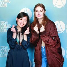 two women standing next to each other in front of a blue wall with the words tokyo comic convention written on it