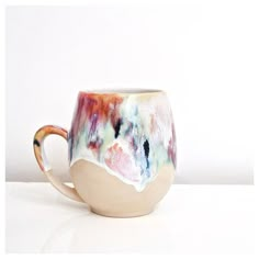 a coffee cup that has been painted with different colors and designs on it, sitting on a white surface