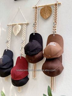 four hats hanging on a wall with chains attached to the hooks and tassels