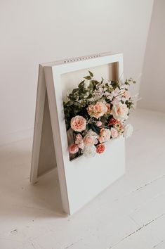 an easel with flowers in it sitting on the floor next to a white wall