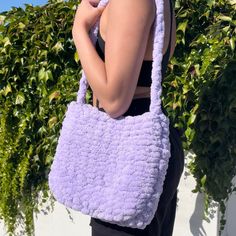 a woman holding a purple crocheted bag in front of her face and looking at the camera