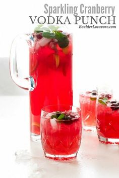 the pitcher is filled with red liquid and garnished with green leaves, surrounded by three glasses