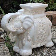 an elephant statue sitting on top of a stone slab in front of some rocks and plants