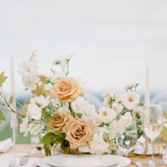 the table is set with white and peach flowers, silverware, candles and napkins