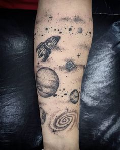 an arm tattoo with planets and stars on the outer half of it, as well as a rocket ship