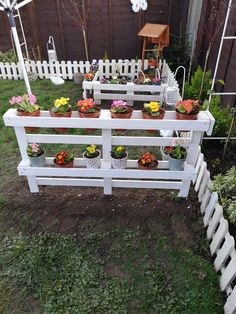 a white bench with potted plants on it in the grass next to a fence