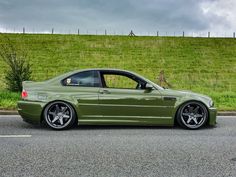 a green car is parked on the side of the road in front of a grassy hill