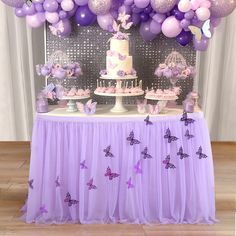 a table topped with a cake and lots of purple balloons on top of the table