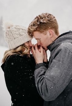 a young man and woman are kissing in the snow while holding each other's hands