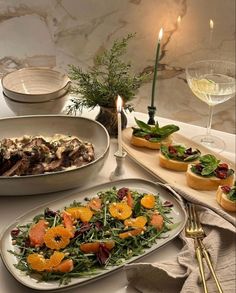 a table topped with plates filled with food next to candles and wine glasses on top of it