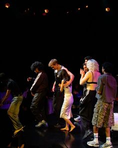 a group of people standing on top of a dark stage with their arms around each other