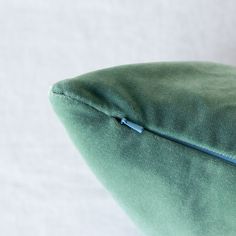 a close up of a green pillow on a white surface with a blue zipper in the middle