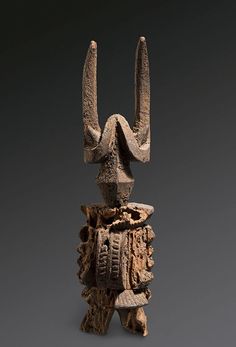 an old wooden sculpture with horns and wheels on it's head, against a gray background