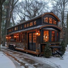 a small house is lit up in the winter with snow on the ground and trees