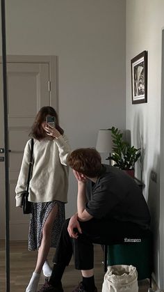 a man taking a photo of a woman sitting on a stool in front of a mirror