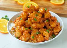 a white bowl filled with orange chicken on top of rice next to sliced oranges