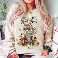 a woman with blonde hair wearing a white christmas sweatshirt and smiling at the camera while sitting on a bed