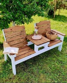 two wooden benches sitting on top of a grass covered field next to a basket filled with flowers