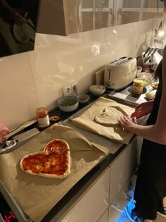 two people making heart shaped pizzas in the kitchen