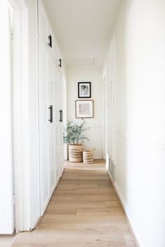 a long hallway with white walls and wood flooring, framed pictures on the wall