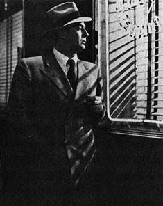 a black and white photo of a man in a suit looking out the window at something