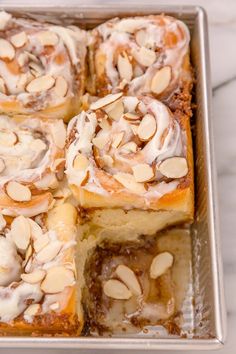 a pan filled with cinnamon rolls covered in icing and almonds on top of a marble counter