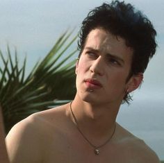 a shirtless young man standing next to a palm tree