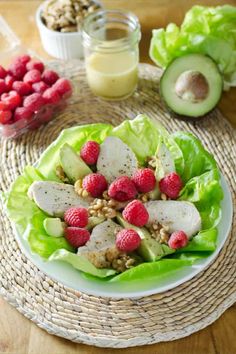 a white plate topped with lettuce, raspberries and avocado