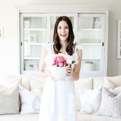 a woman holding a bouquet of flowers in front of a white couch with pillows on it