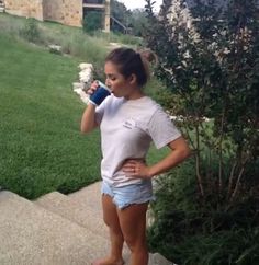 a young woman standing on steps drinking from a cup with her hands behind her back