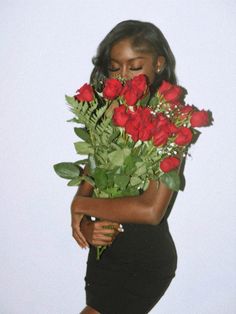 a woman in a black dress holding roses up to her face with both hands on her chest