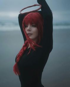 a woman with red hair is standing in front of the ocean holding her arms up