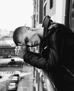 a young man leaning his head on the window sill in front of a city street