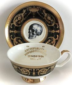 a black and gold porcelain cup with a skull on the side sits next to a plate