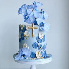 a blue cake with flowers and a cross on the top is sitting on a pedestal