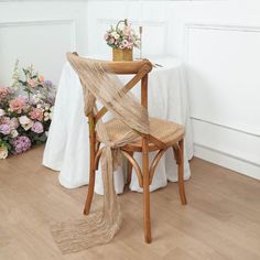 a wooden chair sitting in front of a table with flowers on it and a vase