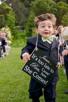 a little boy in a tuxedo holding a sign