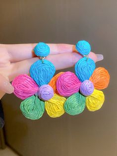 a person holding some colorful yarn balls in their hand and earrings on top of it