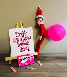 an elf is holding a balloon next to a sign that says don't swallow bubble gum