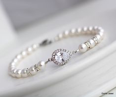 "These dainty yet elegant bracelet is created with a cubic zirconia teardrop and Austrian pearls in ivory/cream.  Pearls measure 6 mm and are accented with rhinestone rondeles for extra sparkle!  Bracelet measures approximately 7 1/2\" long. Focal measures just over  1/2\" long by just under 1/2\" wide.  Please leave your actual wrist measure at checkout to ensure proper fit.  This bracelet is a great gift idea for bridesmaids, mother of the bride, mother of the groom, maid of honor, someone special, or just to spoil your self.  It comes in a white gift box with black ribbon ready to give. This bracelet is created to complement the Audrey collection. Please choose desired pearl color at checkout.      If your dress is ivory I recommend the white color this is an off white and works with wh Pear-shaped Silver Bracelet For Weddings, Silver Teardrop Bracelet For Wedding, Classic Pear-shaped Bracelets For Wedding, Elegant Pear-shaped Bracelet For Wedding, Elegant Pear-shaped Bracelets For Wedding, Cream Pearl Bracelet For Wedding, Adjustable Pearl White Pearl Bracelet For Bridesmaids, White Pearl Embellished Bracelets For Wedding, Bridal Pearl Bracelet