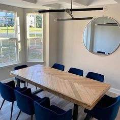 a wooden table surrounded by blue chairs in front of a round mirror on the wall