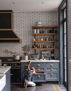 a woman kneeling on the floor in front of a stove top oven next to a counter